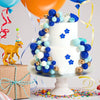 Ein weißes mehrstöckiges Kuchenmodell, dekoriert mit blauen und goldenen Kuglebonbons und Blumen, neben einem gelben Dinosaur