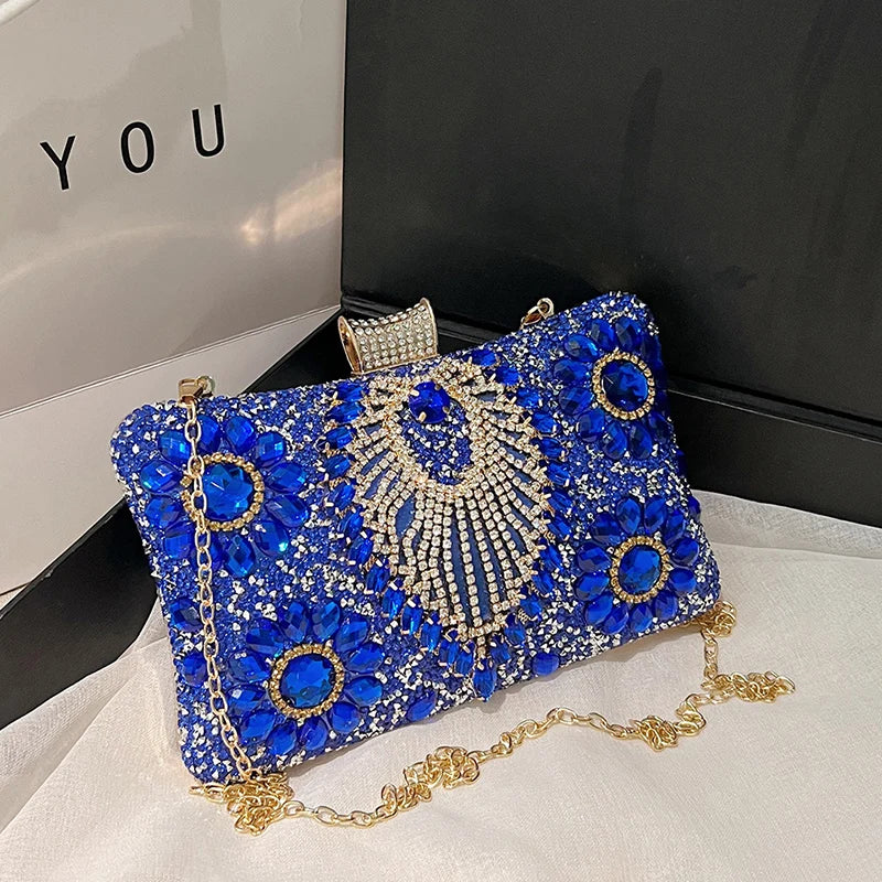 A royal blue rhinestone evening clutch with gold accents and a chain strap displayed on a white surface.