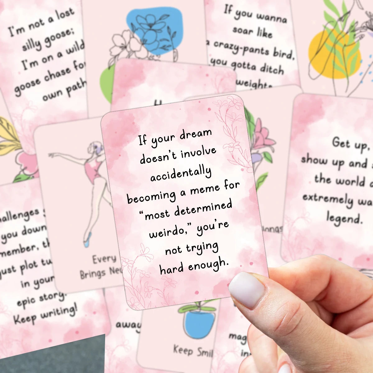Eine Hand hält ein Set rosa Motivationskarten mit positiven Botschaften und Illustrationen.