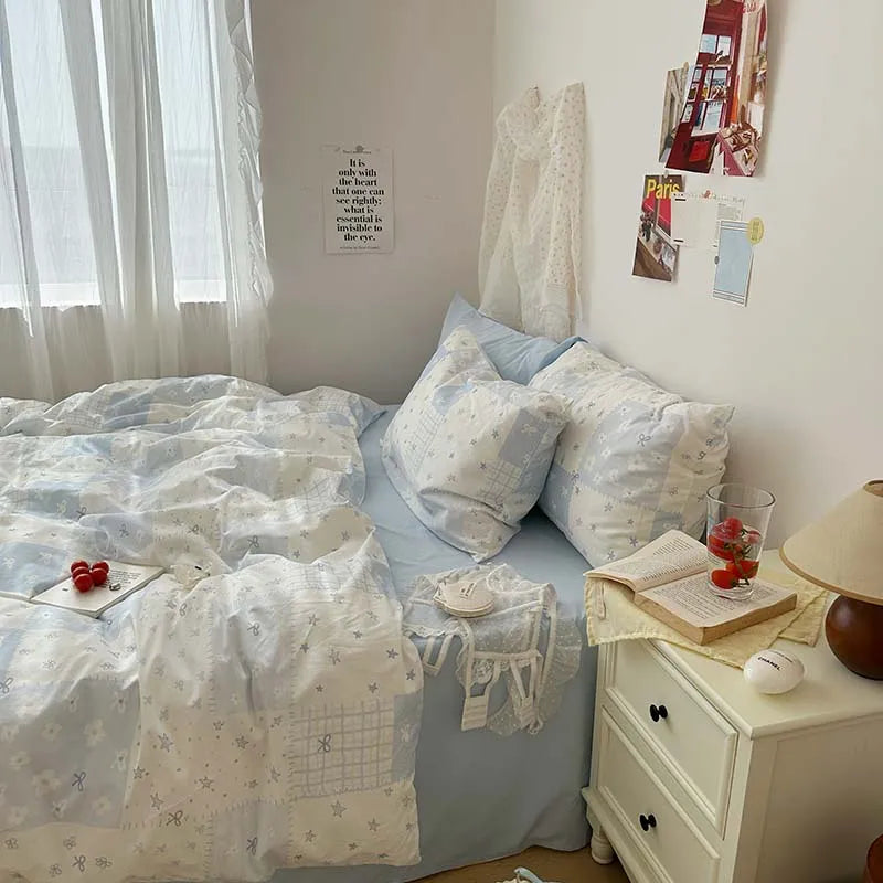 A bed dressed in a blue floral duvet cover set with two matching pillowcases and white curtains.