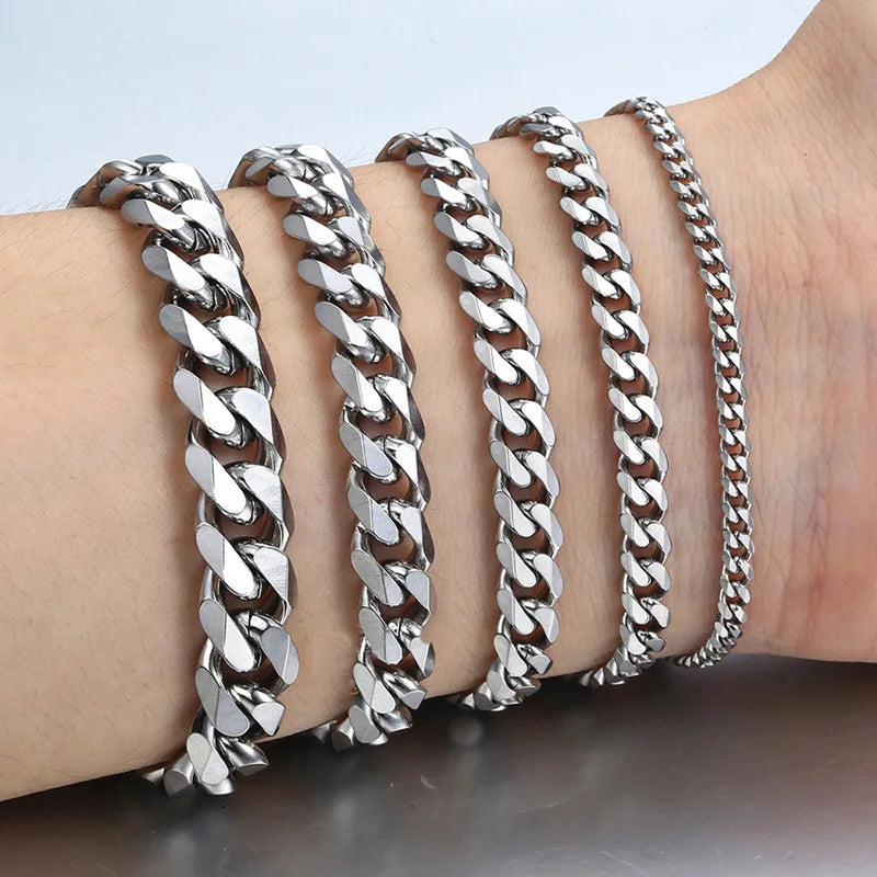 A hand is wearing several silver stainless steel Cuban link bracelets stacked on the wrist.