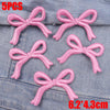 Five pink embroidered bow iron-on patches for DIY clothing decoration displayed on denim fabric.