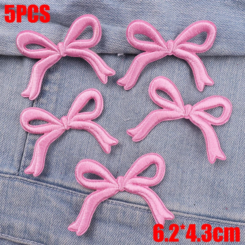 Five pink embroidered bow iron-on patches for DIY clothing decoration displayed on denim fabric.