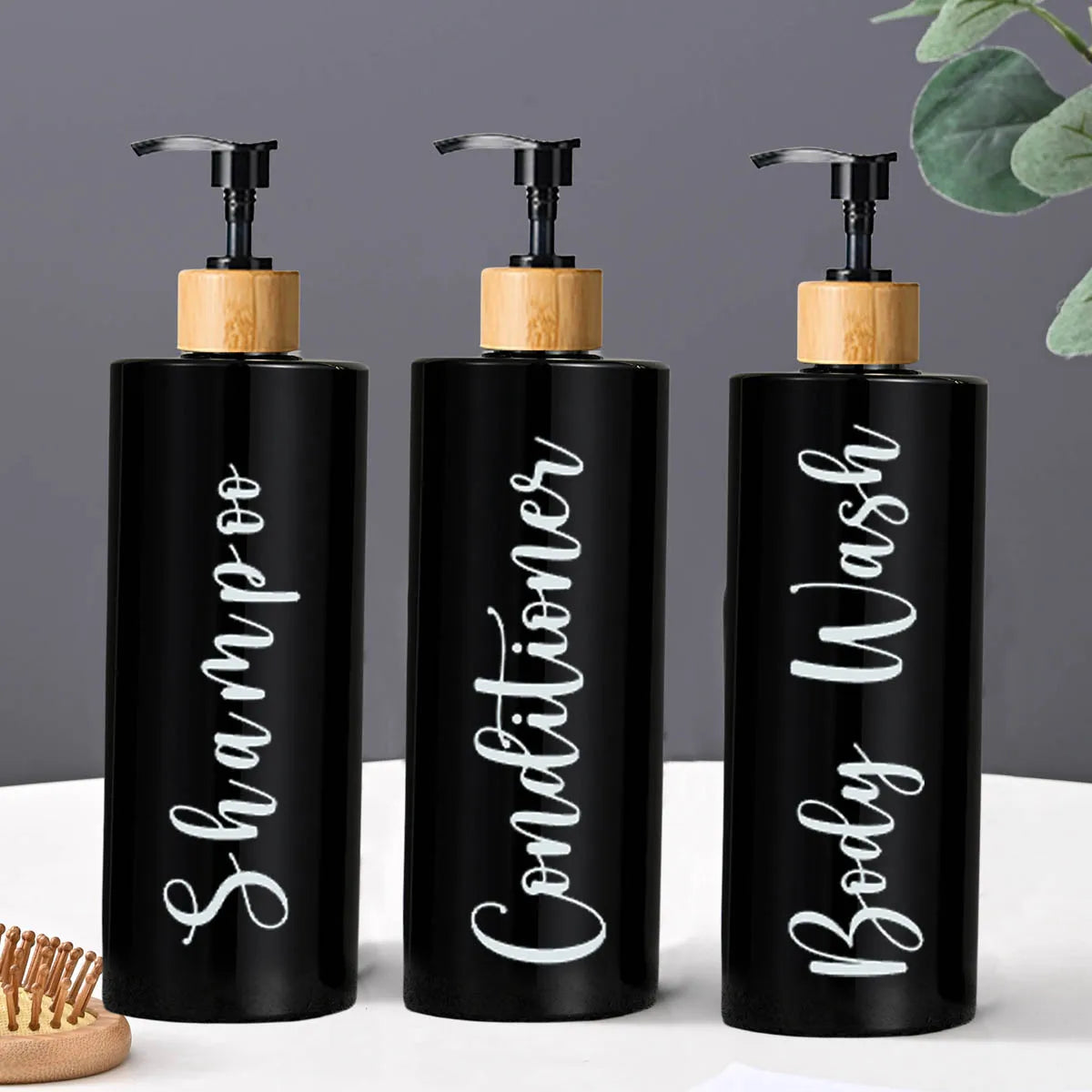Three black glass refillable shampoo and conditioner dispenser bottles with wooden tops