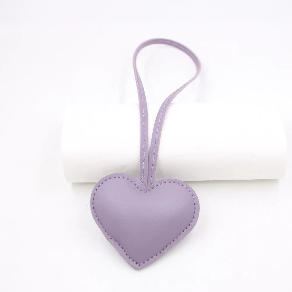 A small lavender heart-shaped PU leather keychain with a loop and a cotton peach charm.