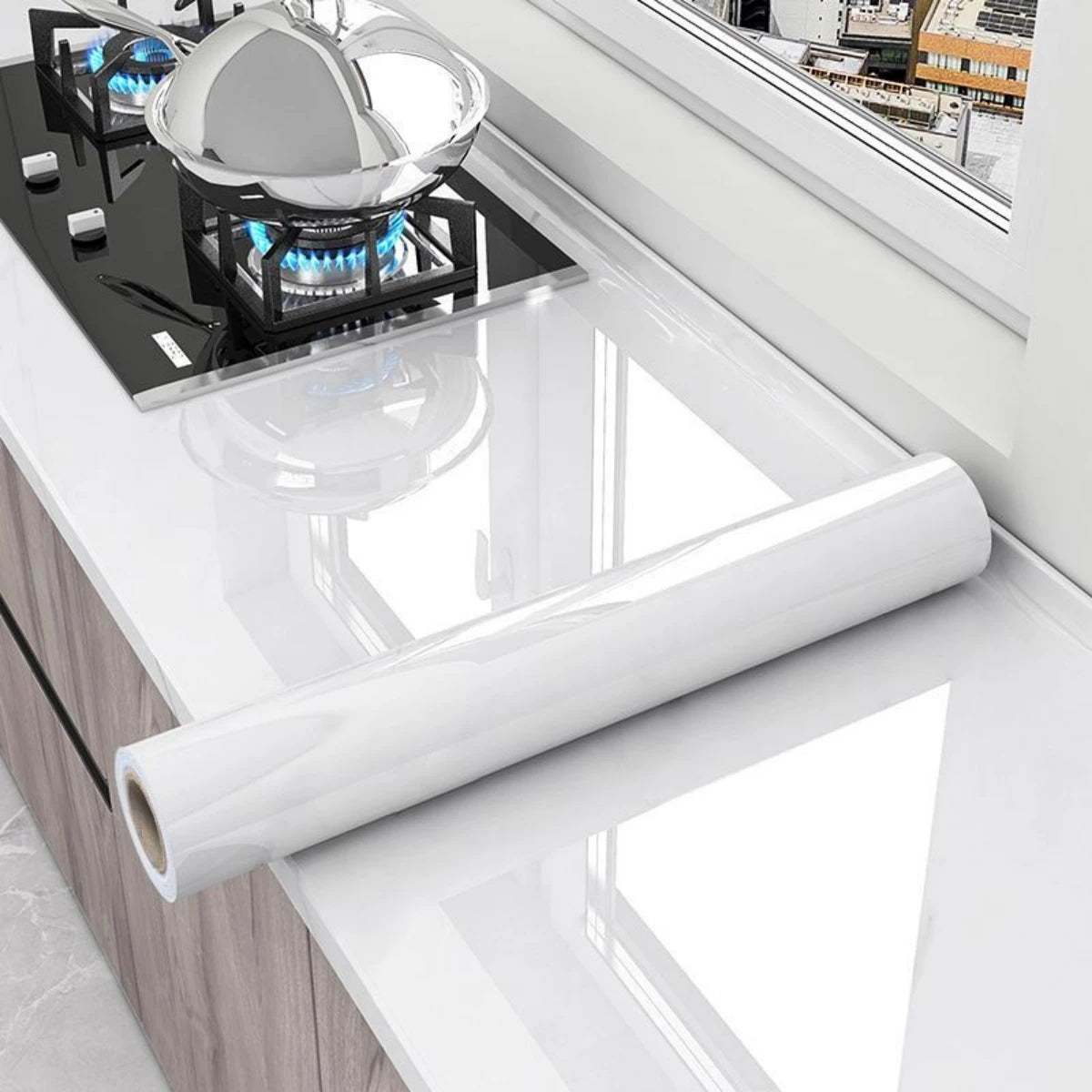 A roll of glossy self-adhesive vinyl wallpaper displayed on a white countertop next to a gas cooktop.