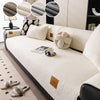 A cream-colored anti-slip lamb fleece sofa mat with decorative round cushions and a small leather accessory on a modern sofa.