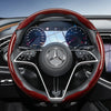 Close-up view of a black steering wheel with red carbon fiber texture covers and Mercedes-Benz instrument cluster.