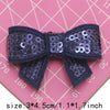 A dark purple sequin bow patch for DIY crafts shown against a pink grid background.