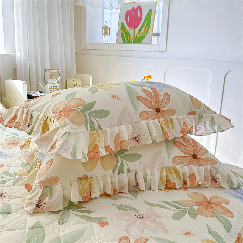 A set of two floral cotton pillowcases featuring peach and green botanical patterns on a bed.