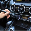 A hand is using a soft bristle interior detailing brush on a car's dashboard and controls.