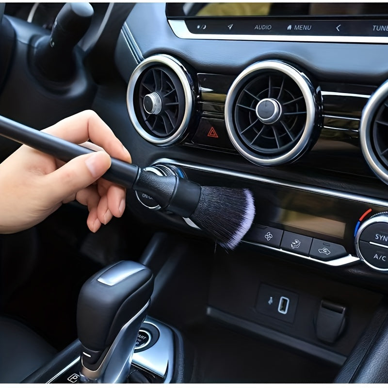 A hand is using a soft bristle interior detailing brush on a car's dashboard and controls.