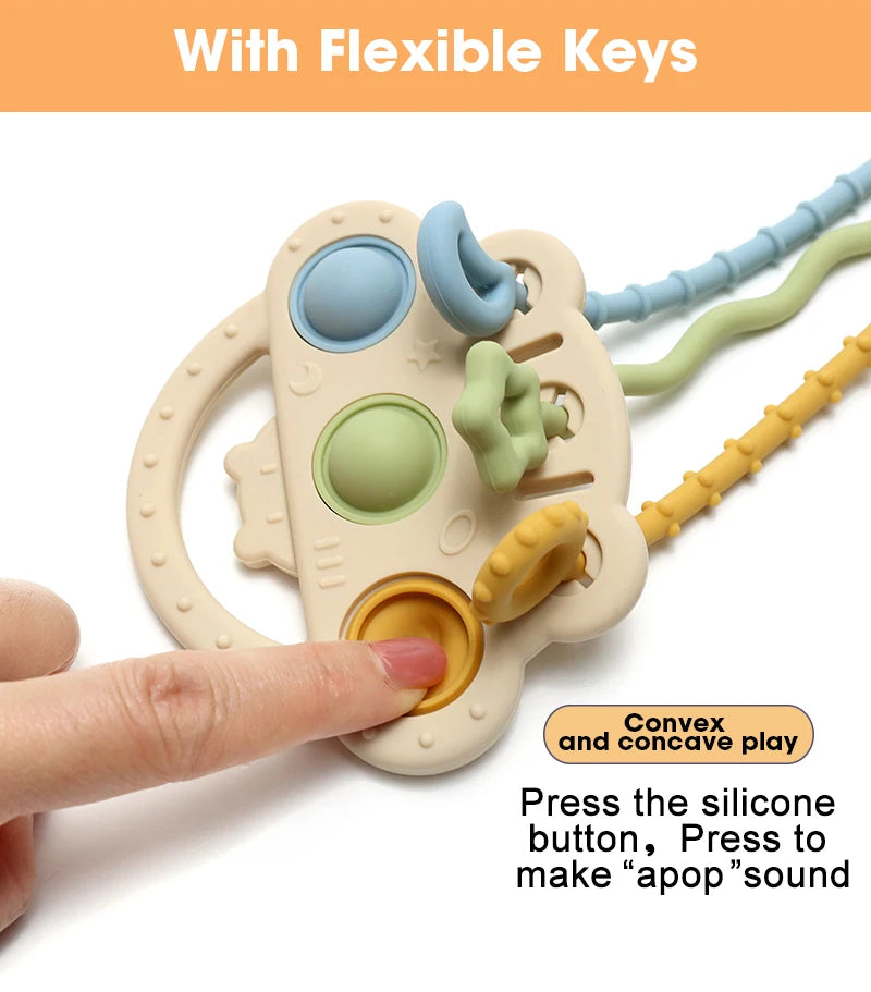 A hand holds a beige silicone bear teether with flexible keys and textured parts for baby play
