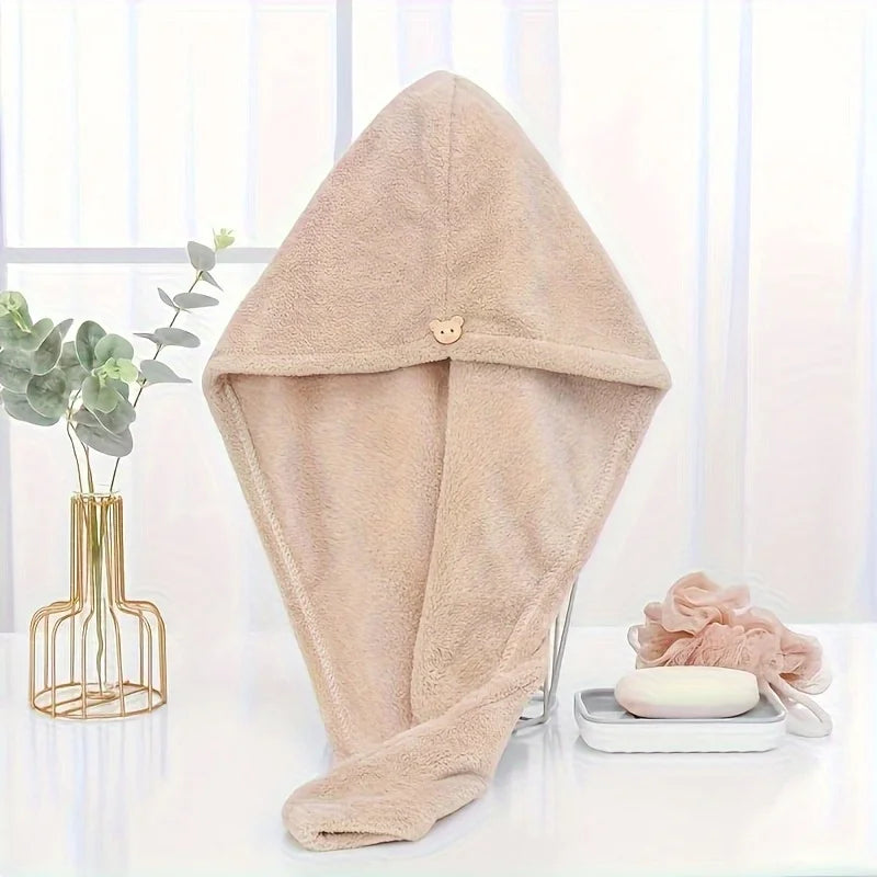 A beige microfiber towel wrap for hair is displayed on a white surface next to a plant and a skincare product.