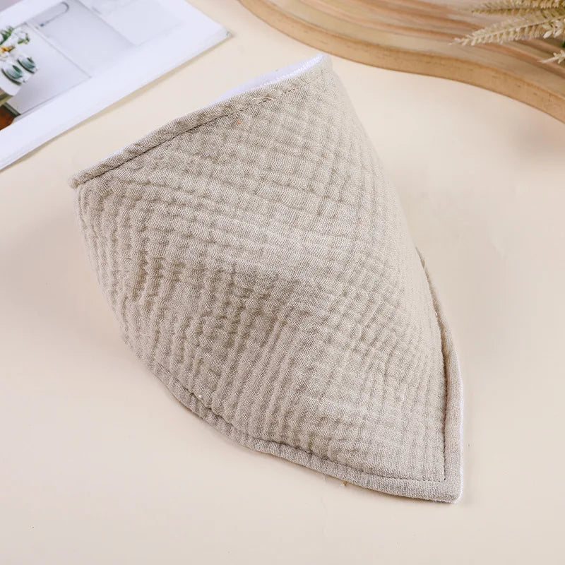 A beige, quilted soft cotton baby bib is shown on a light surface.