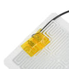 A yellow heating pad component with wires is placed on a white circuit board.