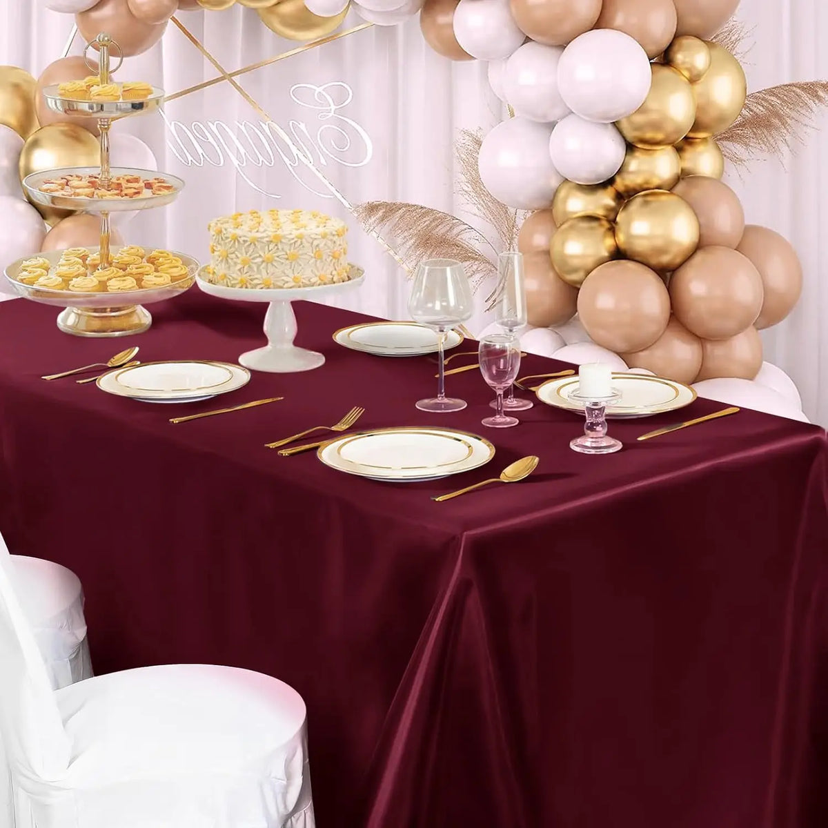 A burgundy satin tablecloth set for an elegant dining event featuring gold and blush balloons and desserts.