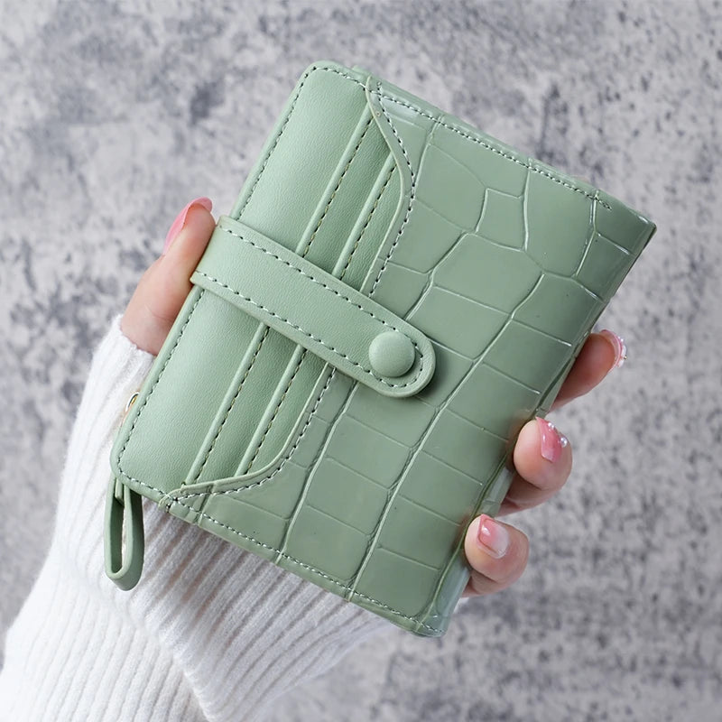 A hand holds a light green crocodile-embossed clutch wallet with a stitched closure.