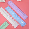 Three portable paper cutters or trimmers in white, light blue, and lavender lying on a pink surface.