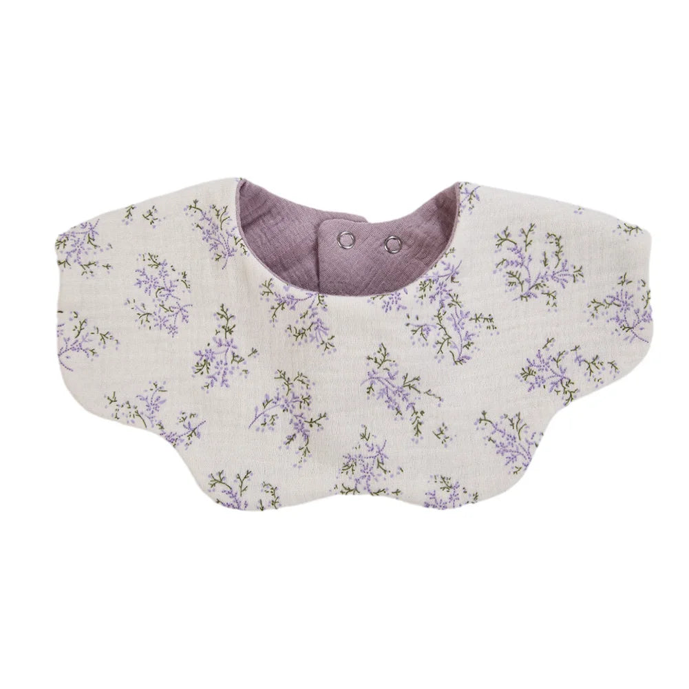 A light beige muslin cotton baby bib with a purple floral print and a gray snap closure.