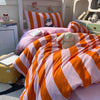 An orange and pink striped duvet cover set with matching pillowcases is displayed on a bed.