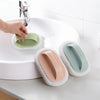 A hand is using a magic sponge scrubber with a long handle to clean a white sink in a bathroom setting.