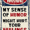 A distressed metal sign with a red oval warning and black text that reads My sense of humor might hurt your feelings