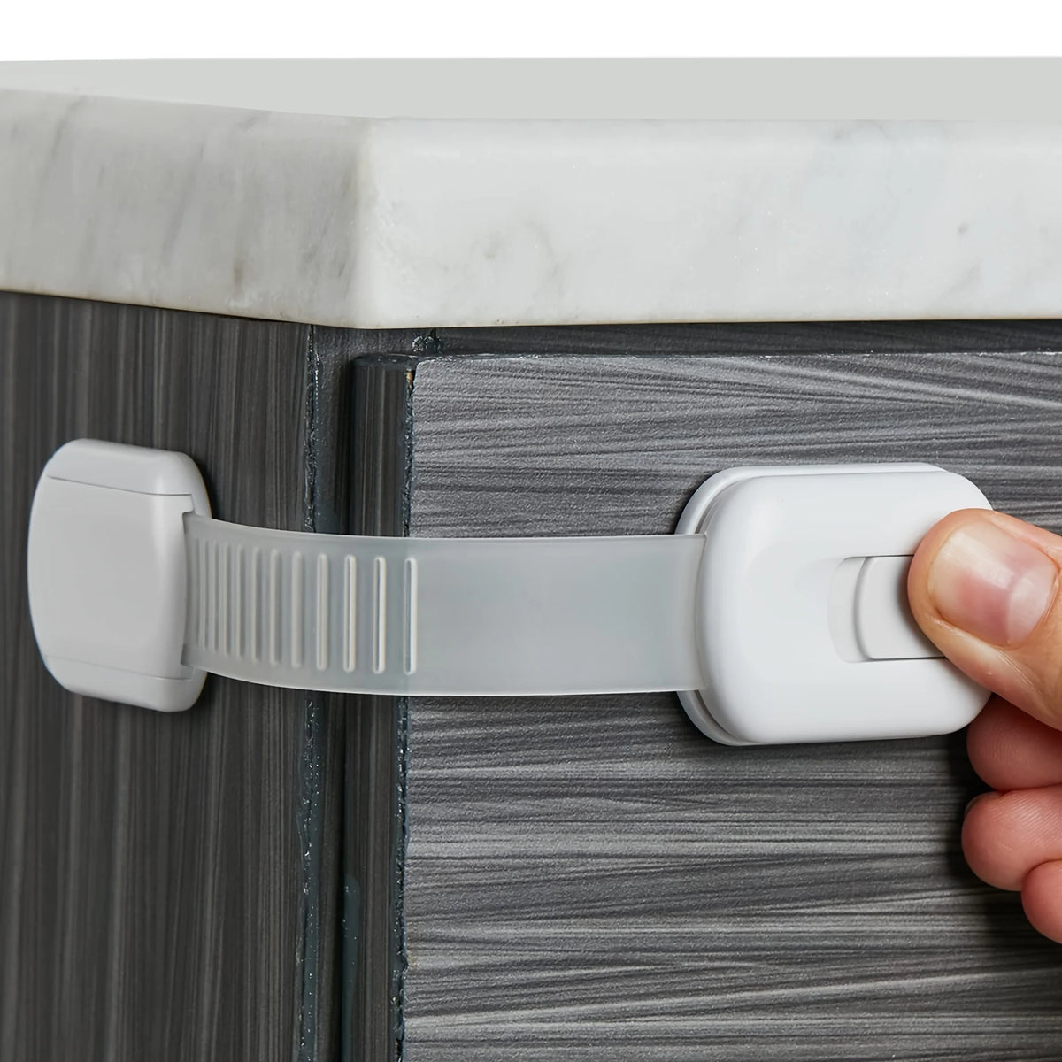 A hand is using an adjustable baby safety lock to open a cabinet door.