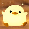 A glowing yellow silicone night light shaped like a smiling chick with black eyes and orange feet.