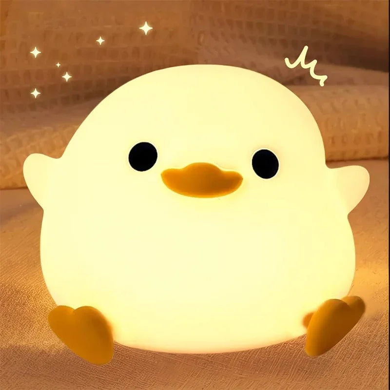 A glowing yellow silicone night light shaped like a smiling chick with black eyes and orange feet.