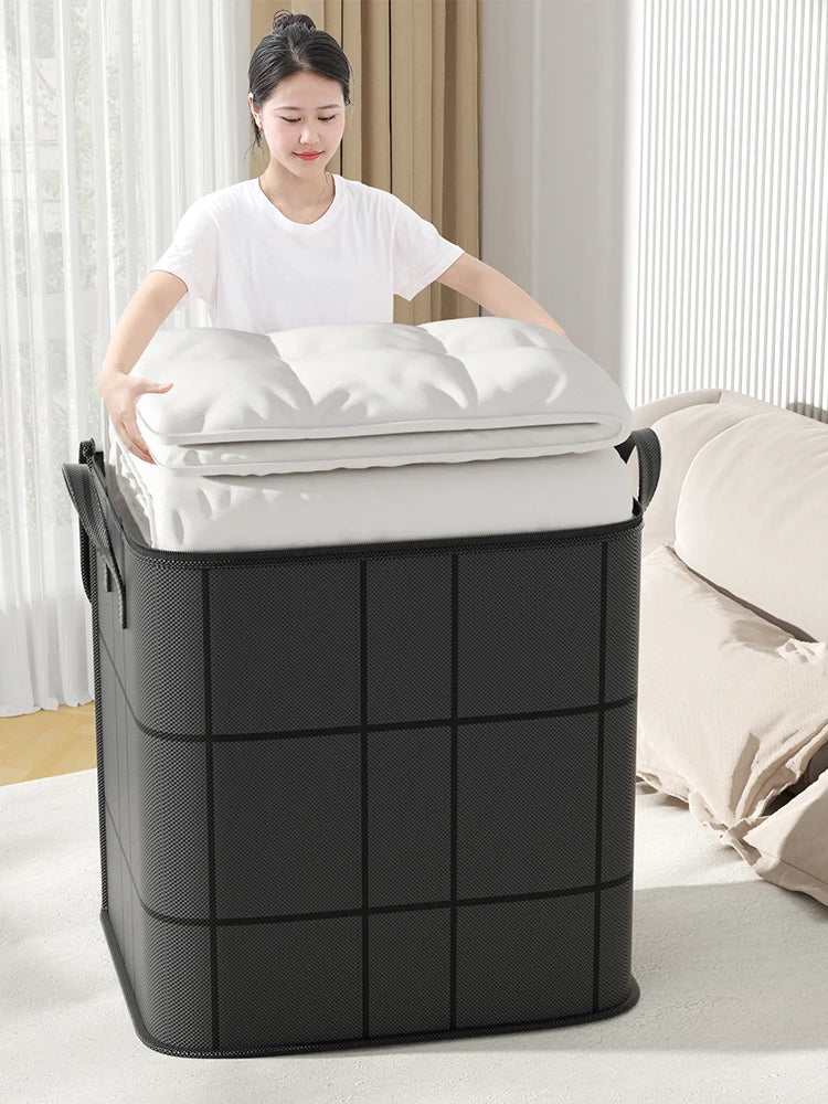 A large black storage bag filled with white pillows and bedding, placed next to a bed.