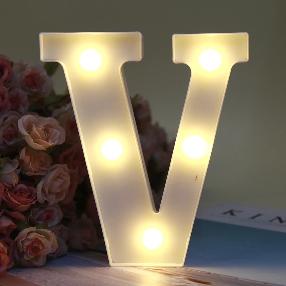 Lumière de nuit alphabet LED blanche en forme de V posée sur une surface en bois à côté de roses roses.