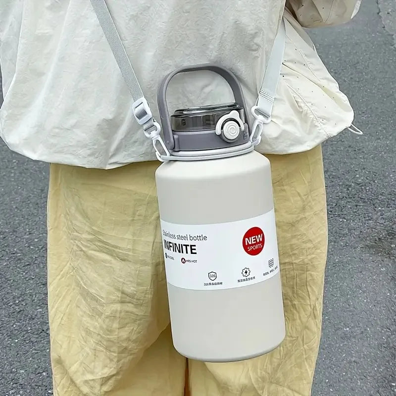A white insulated stainless steel bottle with a silver handle and straw is held by a person wearing light-colored pants.