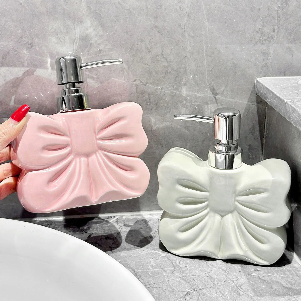 A pink ceramic pump dispenser for bathroom essentials is shown next to a white one on a gray countertop.