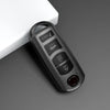 A black TPU car key cover with various buttons and a red lens is shown on a gray surface.