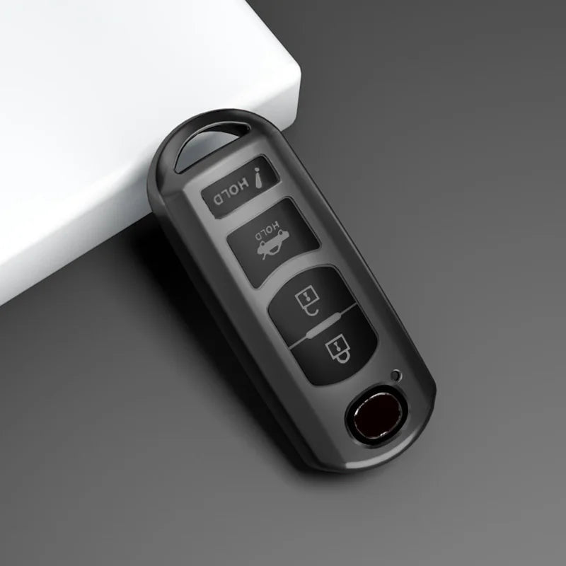 A black TPU car key cover with various buttons and a red lens is shown on a gray surface.