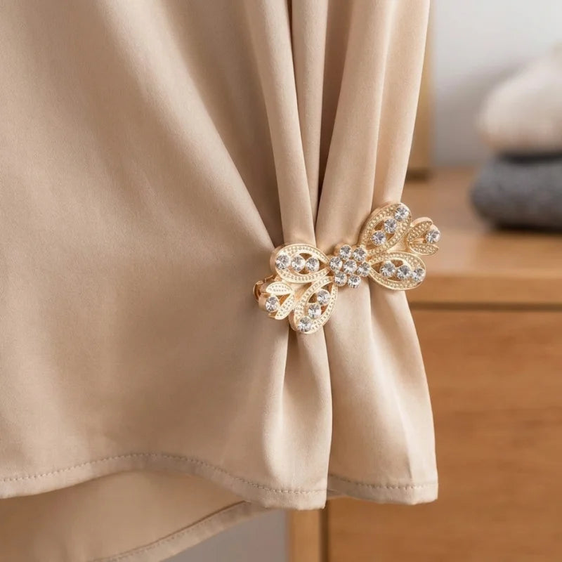 Gold rhinestone bowknot clothing clips securing a beige fabric garment.