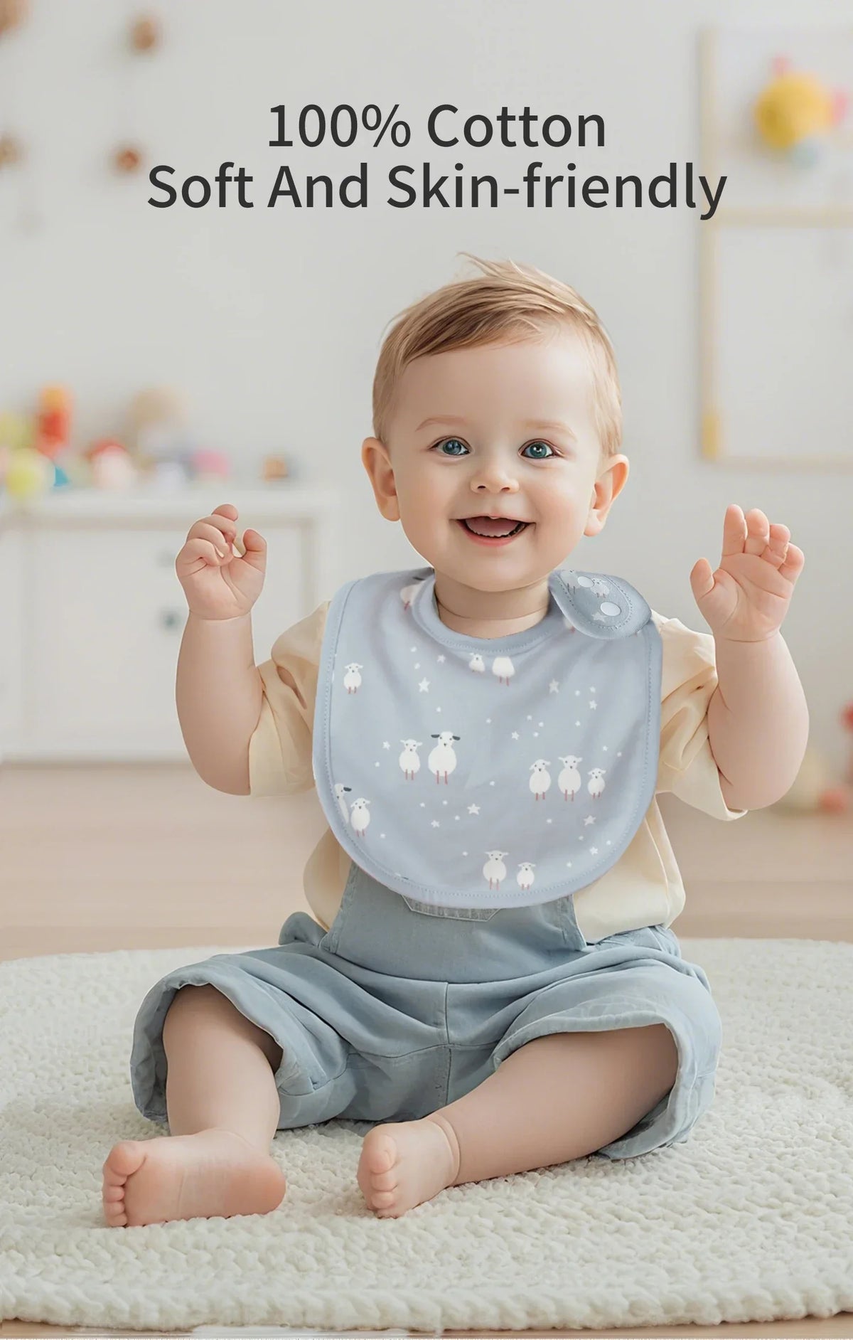 A smiling baby wearing a light blue cotton bib with white flocking, sitting on a white rug.