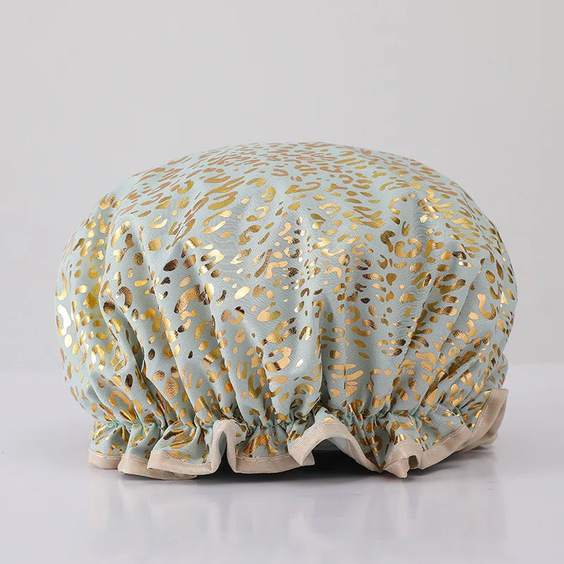 A reusable elastic shower cap for women in a light blue fabric with gold leaf pattern.
