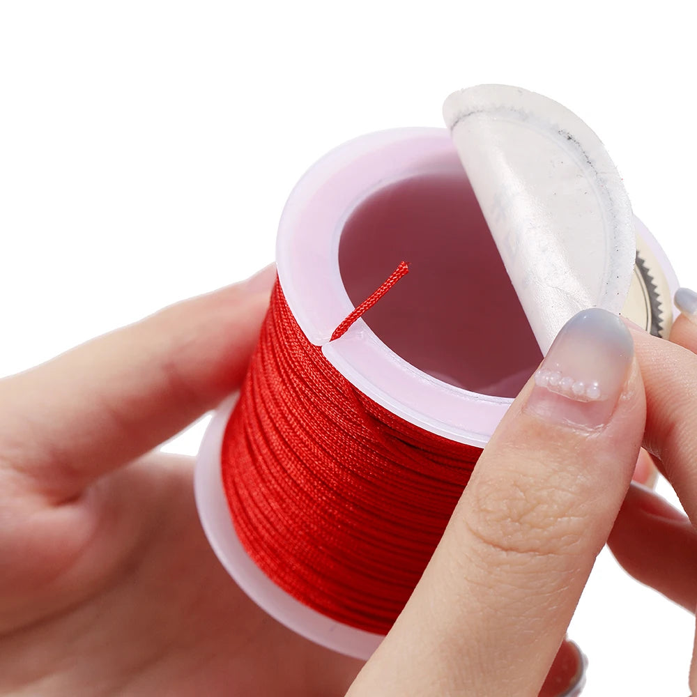 A hand holds a spool of red nylon macramé cord for jewelry making with a pink plastic container.