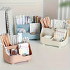A clear acrylic five-compartment desk organizer filled with pens, pencils, and stationery on a white desk.