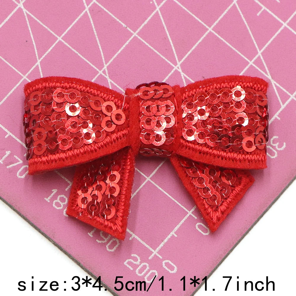 A set of five red sequin bow patches for DIY crafts displayed on a pink grid background.