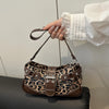 A hand holds a brown leopard print faux leather shoulder bag against a light background.