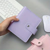 A purple compact cash budget binder with a wallet and zip pocket is held by a hand next to a white computer keyboard and mous