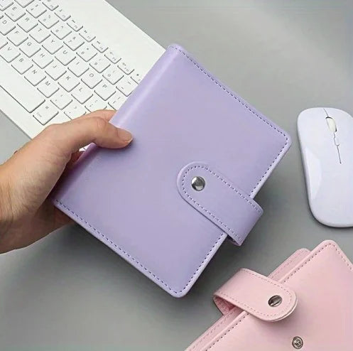 A purple compact cash budget binder with a wallet and zip pocket is held by a hand next to a white computer keyboard and mous