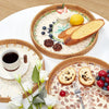 A woven rattan serving tray features a mother of pearl inlay, holding sliced bread and fruit on a white surface.