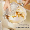 Hands are using a mesh cleaning cloth to remove stains from a non-stick pan.