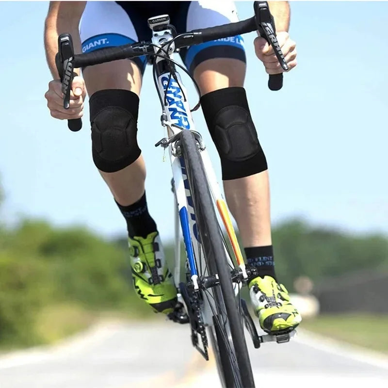 A person riding a bicycle wearing black knee pads and cycling gear on a road.
