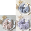 A close-up of soft, fluffy lavender and pink plush coil hair ties displayed on white ceramic plates.