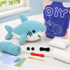 A beginner crochet kit featuring a blue shark amigurumi, yarn, and tools on a white surface.